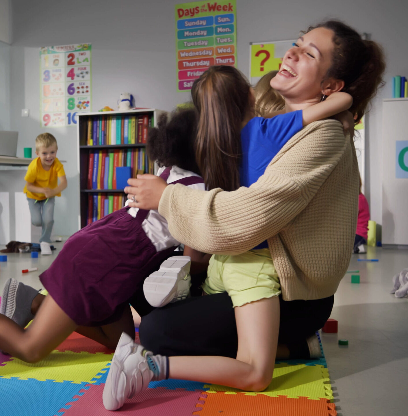 heerful smiling teacher and happy diverse schoolchildren hugging in playroom of kindergarten