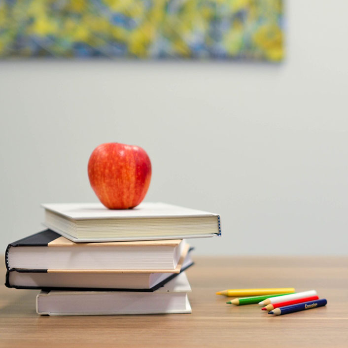 Red apple on stack of study books sitting on a table next to colored pencils