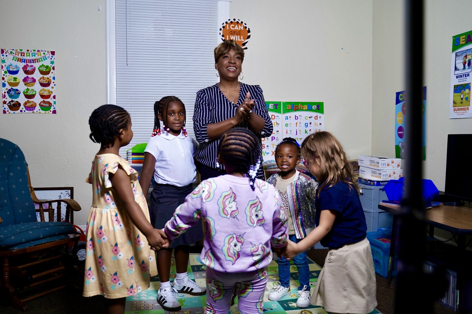 In home child care provider teaching amids preschoolers standing in a circle