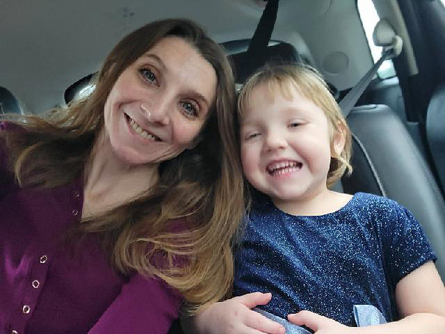 Young mother sitting next to four-year-old daughter, smiling and sitting in car, on their way to child care thanks to Early Learning Scholarship